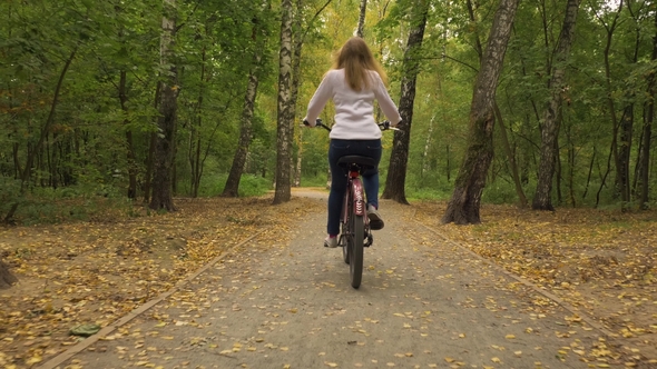 Young Woman Is Riding Bicycle in the Park Autumn and Falling Yellow Leaves alt