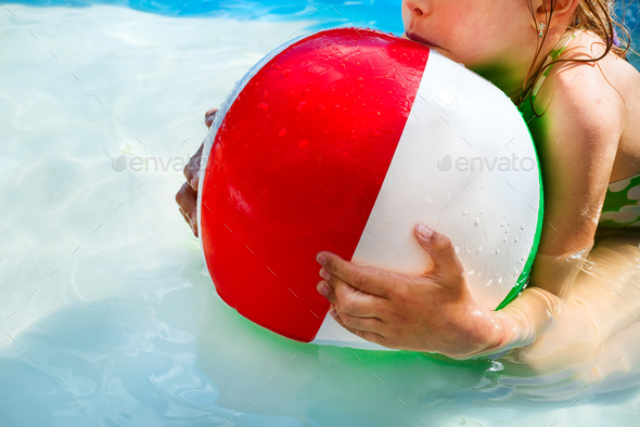 Little girl is playing with a ball in the pool into water on summer vacation in the courtyard - Stock Photo - Images