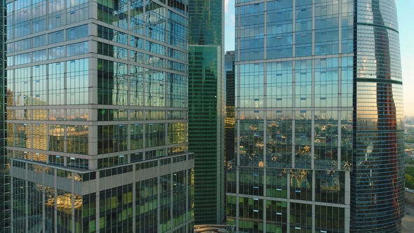 Flying Up Between Two Modern Tall Skyscrapers with Offices and Apartments at Sunrise. Aerial View alt
