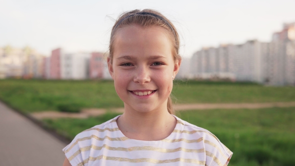 Little Joyful Girl Smiling Against Urban Lawn in Summer Day