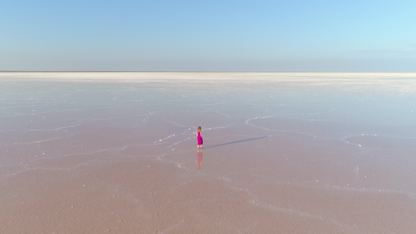 Lonely Woman in Red Dress Is Walking on Water in Huge Salt Lake. Aerial View alt