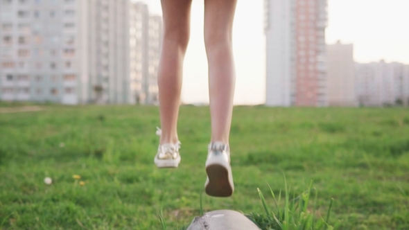 Legs of Little Girl Walking on Concrete Log and Jump on Grass on City Lawn alt