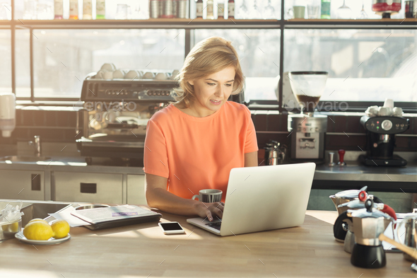 Happy middle-aged woman barista working on laptop - Stock Photo - Images