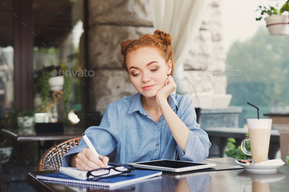 Young redhead girl making notes in a notebook - Stock Photo - Images
