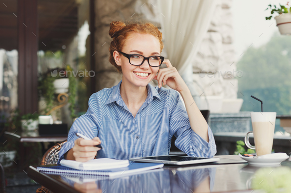 Young redhead girl making notes in a notebook - Stock Photo - Images