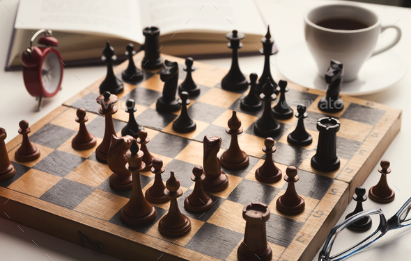 Wooden desk with chess play, book and coffee cup Stock Photo by Prostock-studio