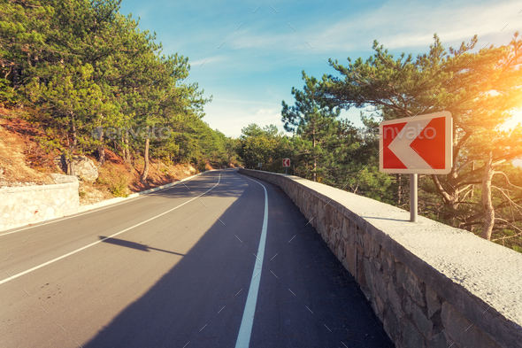 Asphalt road with road sign in the forest at sunrise - Stock Photo - Images