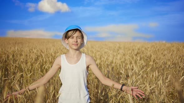 Boy in a Hat Walks on a Golden Wheat Field on a Sunny Day