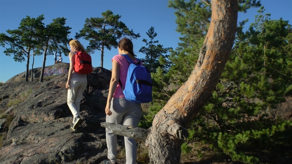 Two Active Young Women Help Each Other To Climb a High Rock alt
