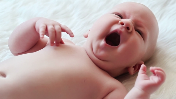 Happy Newborn Baby Yawns  in White Bed