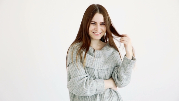 Beautiful Girl of European Appearance in a Warm Sweater Poses Against a White Wall. Emotions