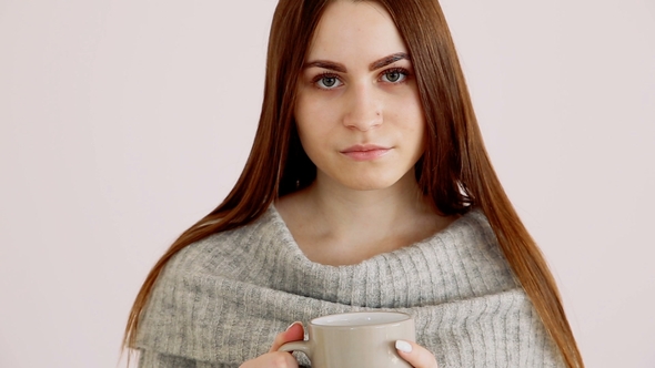 Beautiful Happy Girl of European Appearance in a Warm Sweater Drinks Hot Tea By the White Wall.