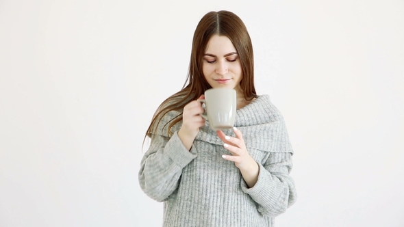 Beautiful Happy Girl of European Appearance in a Warm Sweater Drinks Hot Tea By the White Wall