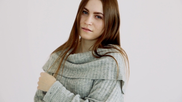Beautiful Girl of European Appearance in a Warm Sweater Poses Against a White Wall