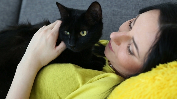 Beautiful Dark-haired Girl with a Black Cat Is Relaxing at Home