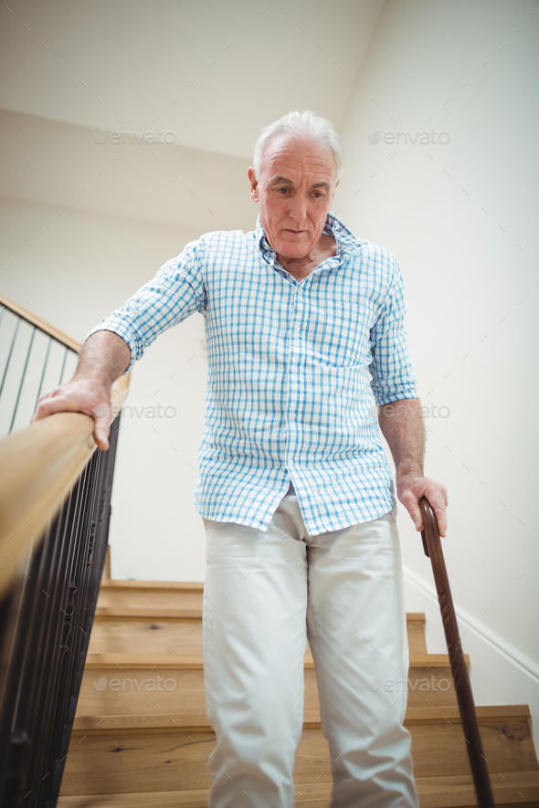Senior man climbing downstairs with walking stick Stock Photo by