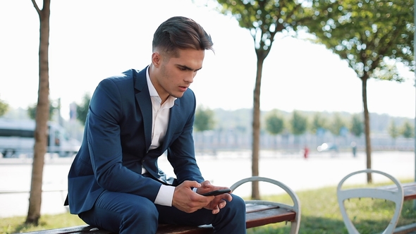 Unhappy Businessman with Smartphone Reading Bad News in on the Bench on the Street alt