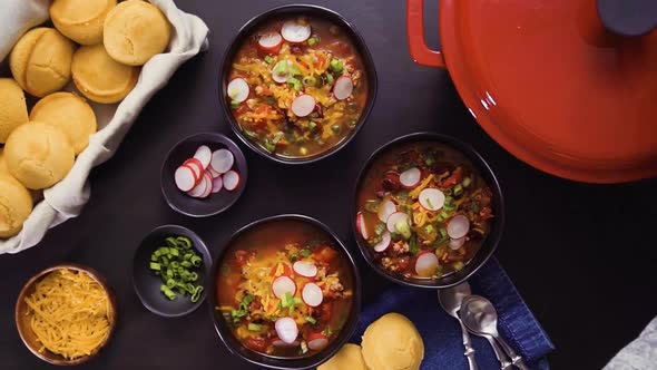 Step by step. Top view. Turkey chili garnished with green onions, radishes, and cheddar cheese in bl alt