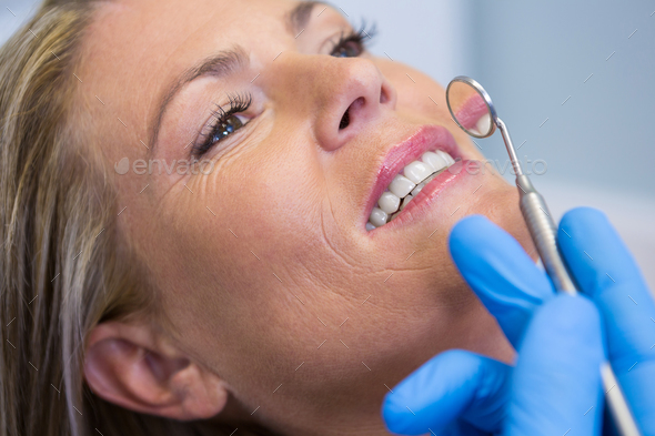 Dentist holding angled mirror by woman at medical clinic Stock Photo by Wavebreakmedia