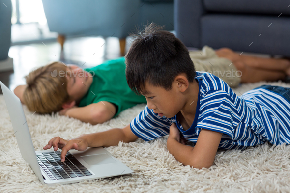 Boy lying on rug and using laptop in living room Stock Photo by Wavebreakmedia