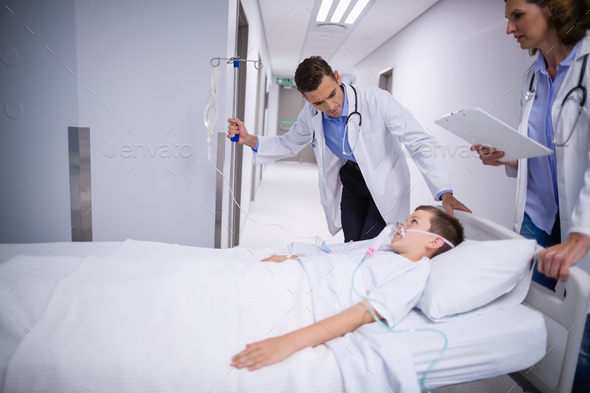 Doctor adjusting iv drip while patient lying on bed Stock Photo by Wavebreakmedia