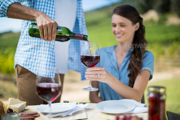 Man pouring red wine in glass held by woman Stock Photo by Wavebreakmedia
