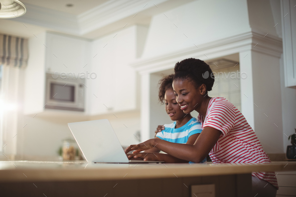 Mother and daughter using laptop in kitchen Stock Photo by Wavebreakmedia