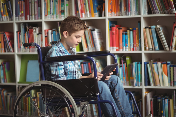 Disabled schoolboy using digital tablet in library Stock Photo by Wavebreakmedia