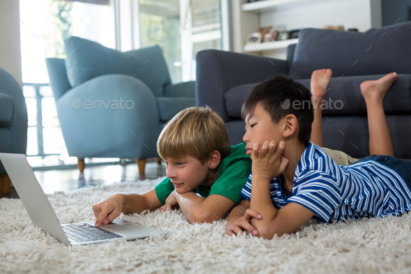Siblings lying on rug and using laptop in living room Stock Photo by Wavebreakmedia