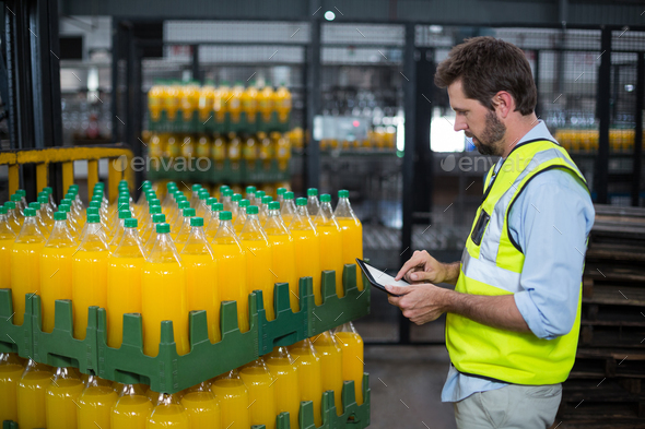 Factory worker maintaining record on juice bottles on digital tablet Stock Photo by Wavebreakmedia