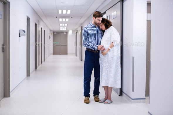 Man comforting pregnant woman in corridor Stock Photo by Wavebreakmedia
