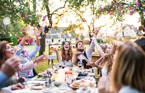 Bride and groom with guests at wedding reception outside in the backyard. Stock Photo by halfpoint