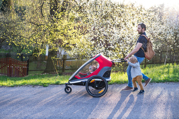 A father with toddler son pushing a jogging stroller outside in spring nature.