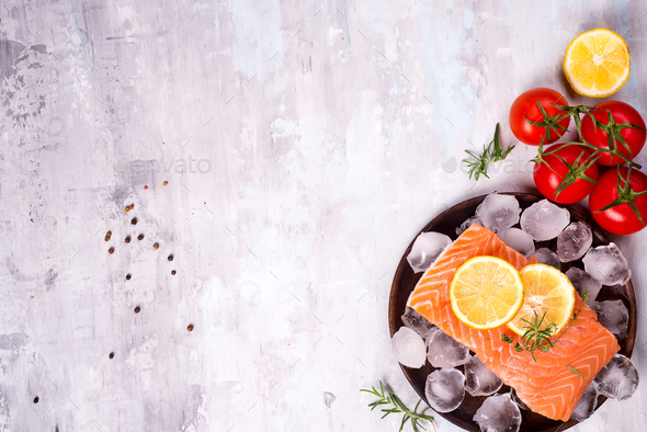 Salmon steaks on ice with lemon slice on wooden plate with tomato - Stock Photo - Images
