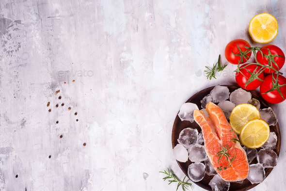 Salmon steaks on ice with lemon slice on wooden plate with tomato - Stock Photo - Images