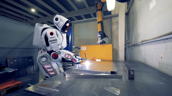 Factory Robot Is Working with Welding Equipment and a Metal Sheet at a Plant alt