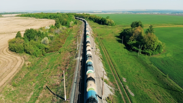 Freight Train with Tank Wagons Goes on a Long Railway Near Fields alt