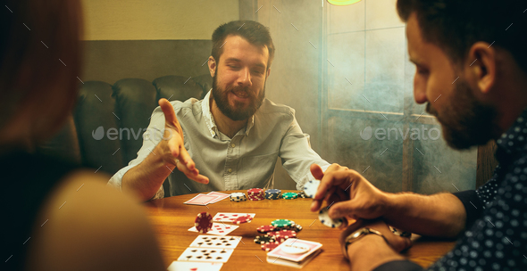 Side view photo of friends sitting at wooden table. Friends having fun while playing board game. Stock Photo by master1305