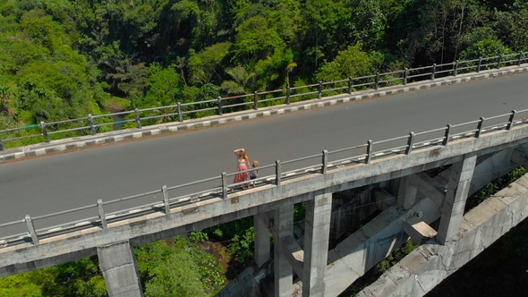 Aerial Shot of a Woman and Her Son Standing on a Tall Bridge Crossing a Canyon with a River on Its alt