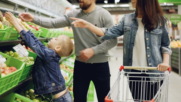 Happy Young Family Mother, Father and Child Are Buying Fruit in Supermarket Putting Pineapple in alt