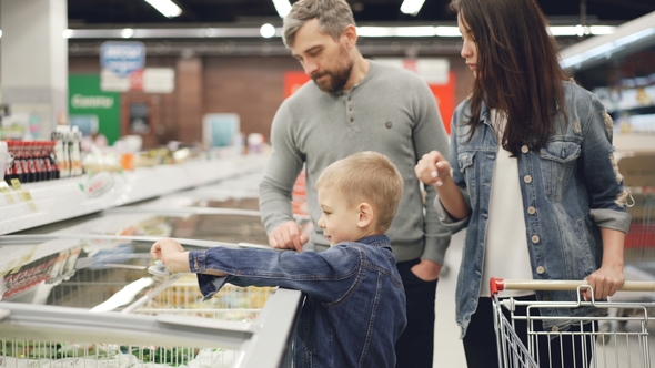 Little Boy Is Opening Freezer and Taking Pack of Frozen Vegetables Then Giving It To His Daddy While alt