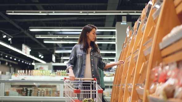 Attractive Girl Customer Is Buying Bread in Bakery Department Is Shop, Smelling It, Smiling and alt