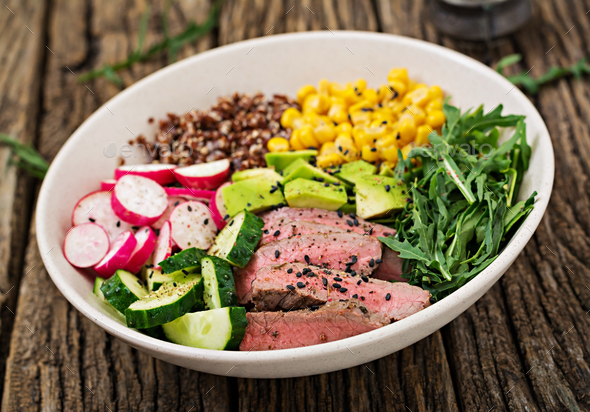 Bowl lunch with grilled beef steak and quinoa, corn, cucumber, radish and arugula Stock Photo by Timolina