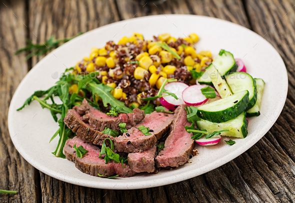 Bowl lunch with grilled beef steak and quinoa, corn, cucumber, radish and arugula Stock Photo by Timolina