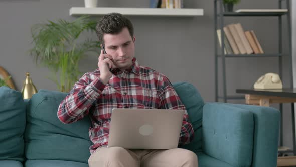 Man with Laptop Talking on Smartphone on Sofa alt