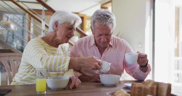 Senior caucasian couple pouring milk in cereal bowl having breakfast together at home alt