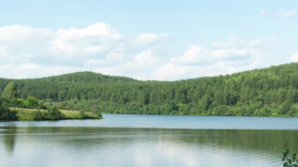 Beautiful Clouds Move Over a Body of Water and Wooded Mountains on a Summer Sunny Day alt