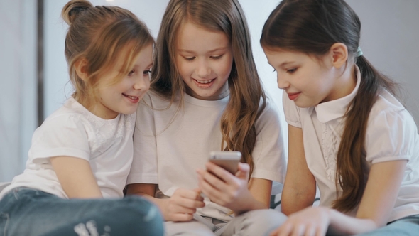 Beautiful Little Girls Are Sitting on the Couch and Showing Her Something Interesting alt