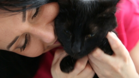 Love for Pets. Beautiful Dark-haired Girl with a Black Cat Is Relaxing at Home in the Bed Room