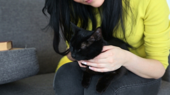 Love for Pets. Beautiful Dark-haired Girl with a Black Cat Is Relaxing at Home in the Living Room